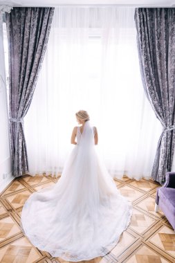 Şık elbiseli bir gelin kameraya arkası dönük durur.