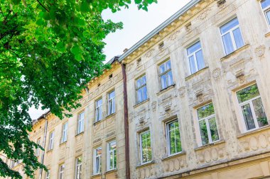 Şehir caddesinde pencereleri ve yeşil yapraklı ağaçları olan eski bir bina..