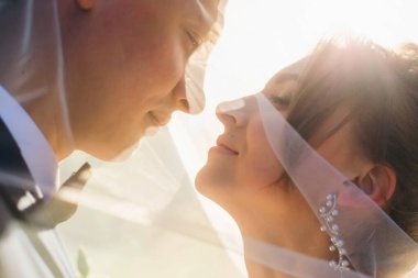 Gelin ve damat birbirlerine bakıyorlar ve burunlarını eğiyorlar. Düğün duvağına bürünmüş yeni evlilerin profili.