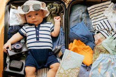 Küçük çocuk bir bavulun içinde kıyafetlerle yatıyor. Tatil gezisi için bagajda bir çocuk, fotokopi odası. Bir yaşın altındaki çocuk (12 aylık))