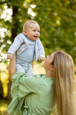 Açık havada mutlu ve uyumlu bir aile. Anne bebeği kusuyor, gülüyor ve yazın doğada oynuyor.