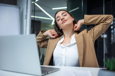Sakin bir iş kadını rahat ofis sandalyesinde ellerini uzatıyor elleri başının arkasında mutlu bir kadın işten sonra tatmin oluyor, gözleri kapalı tatilin tadını çıkarıyor.,