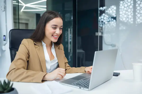 Young and happy caucasian woman working in modern office using laptop, businesswoman smiling and feeling happy