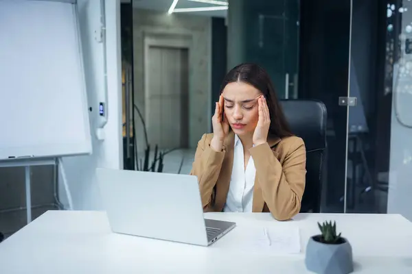 Exhausted female worker sit at office desk feel unwell, tired woman employee suffer from migraine or headache unable to work. Health problem concept