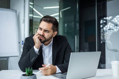 Masada dizüstü bilgisayar kullanarak oturan üzgün ve sıkılmış bir iş adamının portresi. Stresli adamın iş sorunları var.