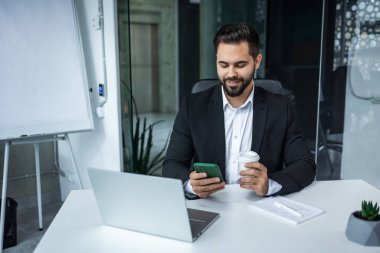 Meşgul iş adamı cep telefonu ve dizüstü bilgisayar kullanır ve kahve fincanı tutar..