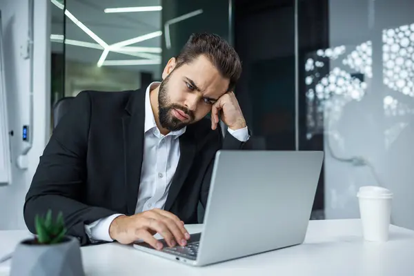 厌倦了懒洋洋地打瞌睡的大胡子男性经理厌倦了在办公室的电脑上工作项目 免版税图库照片