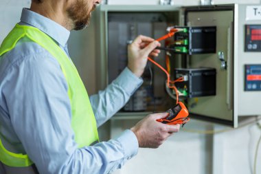 Handsome electrician holding multimeter near electrical distribution box
