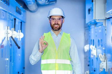 Young handsome technician man wearing uniform and security helmet smiling positive doing ok sign with hand and fingers. Successful expression.