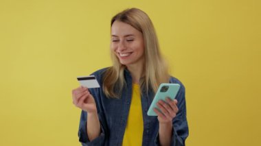 İnternetten alışveriş yapan genç bir kadın cep telefonu kullanıyor ve sarı arka planda kredi kartı bilgilerini daktilo ediyor. Kara Cuma satış günü konsepti