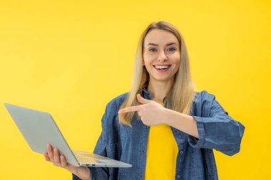 Sarı arkaplanda izole edilmiş ekranda dizüstü bilgisayar kullanan heyecanlı genç kadının portresi