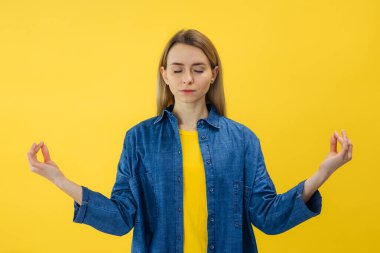 Düşünceli, barışçıl bir kadın meditasyon yapıyor, ellerini Mudra jestinde tutuyor, gözleri kapalı, rahatlıyor, yoga işaretinde parmaklarını tutuyor, sarı duvarda izole edilmiş.