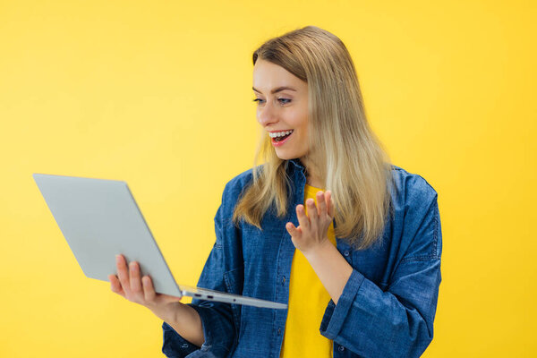Young excited smiling caucasian student freelancer woman using laptop for remote work, e-learning at university college, e-banking, online shopping isolated on yellow background