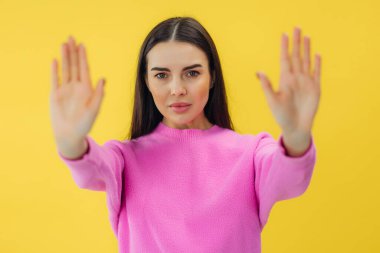 Genç esmer kadın sarı arka planı izole ederek iki eliyle şarkı söylemeyi kesti. Yüzünde olumsuz ve ciddi bir jest olan uyarı ifadesi.