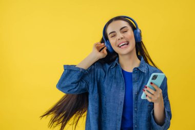 Elinde modern akıllı telefon ve kablosuz kulaklıkla neşeli bir şekilde dans eden ve müzik dinleyen esmer bir kadın.