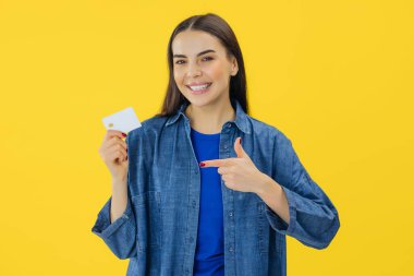 Beyaz banka kartının üzerinde işaret parmağıyla işaret eden gülümseyen beyaz kadın portresi sarı arka planda duruyor. Kadın esmer, uygun alışveriş için nakit ödemeyi öneriyor..