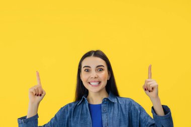 Yukarıdaki pozitif esmer kadın, reklam metniniz için yer gösteriyor. Gülümsemeler sarı arka planda hoş bir şekilde izole edilmiş..