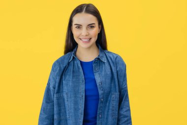 Sarı arka planda izole edilmiş kameraya bakan gülümseyen kadın portresi