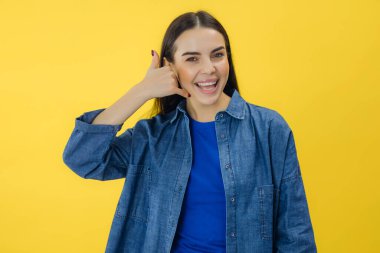 Young happy caucasian woman doing phone gesture like says call me back isolated on yellow background studio portrait clipart