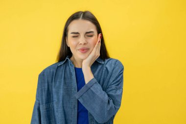 Şiddetli diş ağrısı çeken, avuçlarını yanaklarına bastıran, güçlü ağrılar yüzünden gözlerini kapatan, sarı arka planda izole edilmiş genç bir kadın.