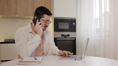 Genç işadamı akıllı telefondan konuşuyor ve dizüstü bilgisayar kullanıyor.