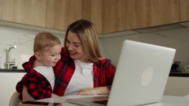 Mutlu anne ve şirin çocuk uzaktan video çekiyor kameraya el sallıyor, sevgi dolu anne ya da bebek bakıcısı ve çocuk gülümsüyor webcam kaydında konuşuyorlar ve internetten iletişim kuruyorlar.