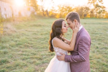 İki yeni evli genç gün batımının arka planında bir öpücüğün önünde durup sarılıyorlar..