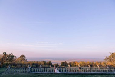 Güzel, romantik bir düğün. Yeni evliler. Eski kalenin yakınlarında sarılıyorlar.