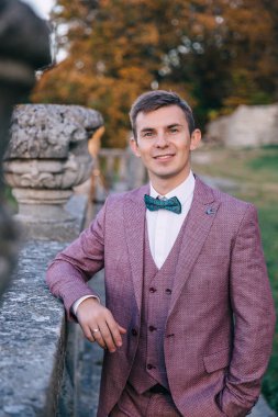 Mor takım elbiseli şık bir genç adam gülümsüyor, doğada yürüyor..