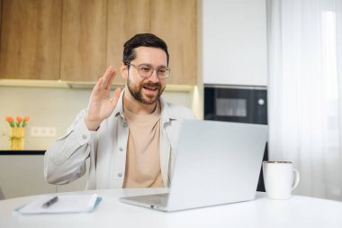 Duygusal, genç, beyaz bir adam ev bilgisayarında uzaktan görüşme yapıyor. Çevrimiçi video görüşmesi sırasında el sallayarak selam vermek.