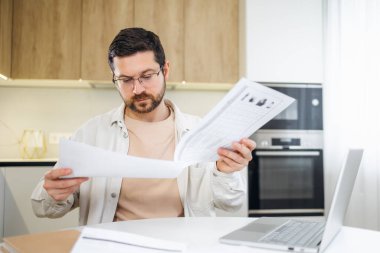 Kafası karışmış genç adam kötü mali rapor okuyor evden uzaktan çalışmayı analiz ediyor.