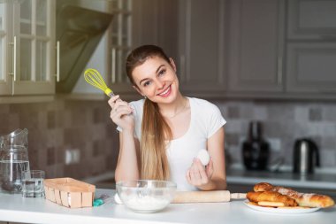 Aşçı kız çırpı ve yumurtayla mutfakta duruyor.