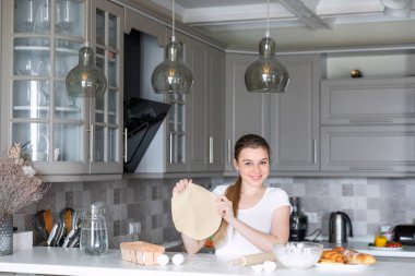 Pizza hamuru tutan kız. Masa yumurtasındaki malzemeler, un, bir sürahi su, sallanan hamur.