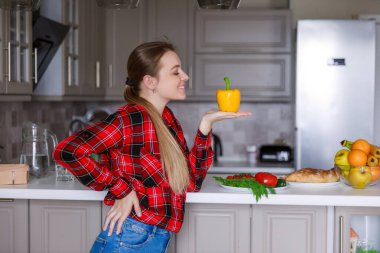 Mutfakta masanın yanında duran ve elinde biber tutan genç bir kadın.