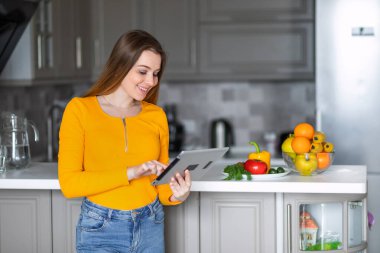 Turuncu kazaklı bir kız sağlıklı yemek tarifi için elinde tablet tutuyor.