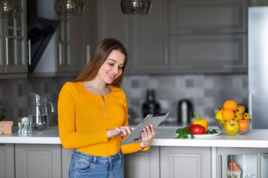 Turuncu kazaklı bir kız sağlıklı yemek tarifi için elinde tablet tutuyor.