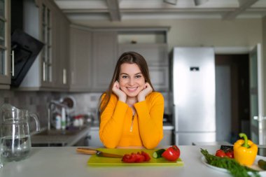 Mutfaktaki masada duran genç kadın. Masada taze meyve ve sebze var..