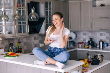 Sevimli, sevimli, neşeli, şık, modaya uygun bir kız modern beyaz mutfakta müzik dinliyor..