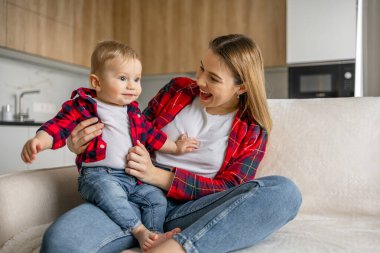 Mutlu anne kucağı küçük oğlu gülüyor kanepede oturuyor ev mutfağında