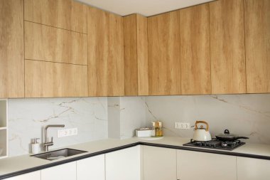 Çağdaş mutfak tasarımı. Ahşap dolaplar, mermer kaplama ve paslanmaz çelik eşyalar. Minimalist dekor ve temiz çizgiler modern yaşam ve yemek pişirmek için ideal, parlak ve işlevsel bir alan yaratıyor..