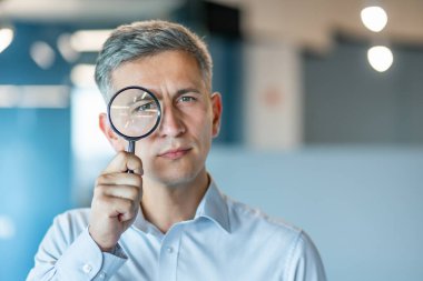 Resmi gömlekli profesyonel bir özel dedektif modern ofis ortamında büyüteçle merakla inceler. Araştırma temaları, detaylara dikkat, ve merak, araştırma, analiz ve keşif.