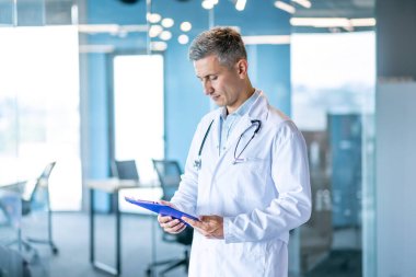 Beyaz önlük giyen profesyonel bir doktor ve steteskop hasta kayıtlarını modern bir hastanenin panosunda inceliyor..
