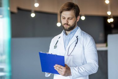 Beyaz önlüklü profesyonel bir doktor modern bir klinik hastanesinde mavi bir panoyu inceliyor..