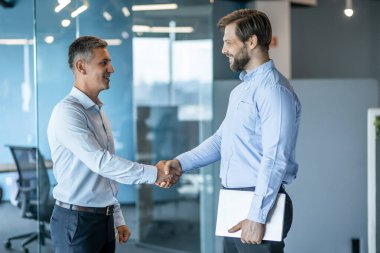 Modern bir ofis ortamında iki profesyonel iş adamı el sıkışır. Başarılı iş anlaşması veya ortaklık, profesyonellik, işbirliği ve karşılıklı saygı