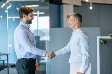 Ofis ortamında el sıkışan iki işadamı, profesyonellik, ortaklık ve başarı.