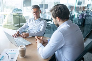 Modern bir ofiste oturmuş, ciddi tartışmalar yapan iki işadamı. dizüstü bilgisayar ve belgeler, iş toplantısı, takım çalışması, iletişim ve kurumsal strateji