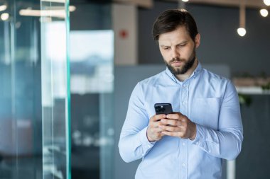 Modern ofis ortamında akıllı telefonunu dikkatle kullanan mavi gömlekli profesyonel bir iş adamı. konsantrasyon, profesyonel iletişim.