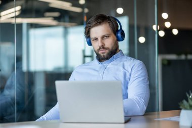 A focused man wearing headphones is working on a laptop at an office desk, reflecting concentration and productivity in a modern workplace setting.