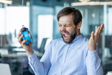 Mavi gömlekli sakallı bir adam elinde mavi alarmlı bir saat tutarken sevinçten havalara uçuyor. Başarı ve zaman yönetimi, üretkenlik ve motivasyon temaları.