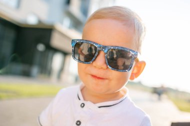 Güneşli bir günde güneş gözlüğü takan çekici bir çocuk dışarıda duruyor. Sıcak bir günde çocukluk eğlencesi ve tasasız bir zevk.